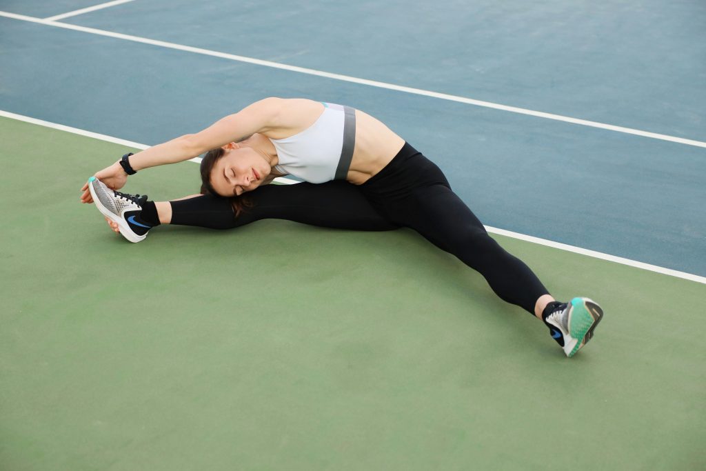 Woman stretching, leaning to one side to grab her shoe, on tennis courts.