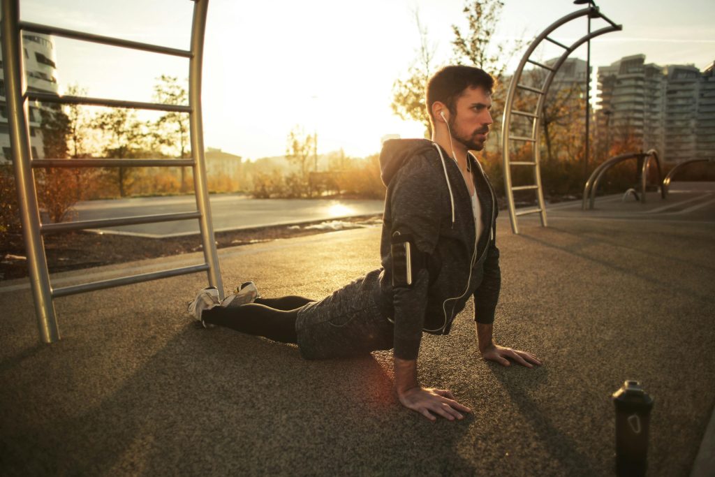 Guy performing the cobra stretch on the ground with the sun behind him.