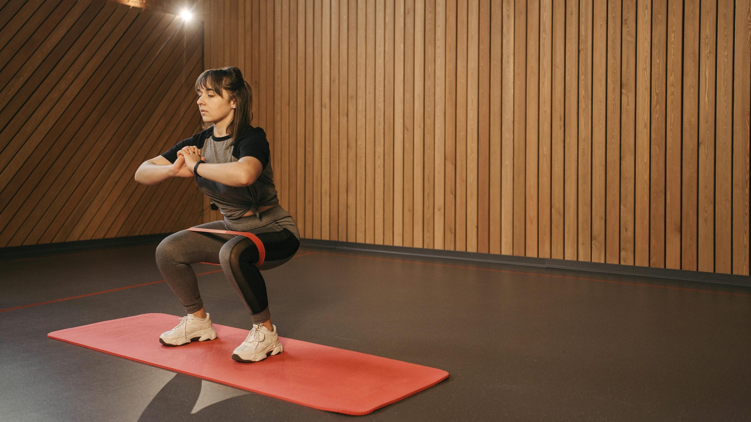 Girl doing a squat in a relatively empty room with a resistance band around her legs.
