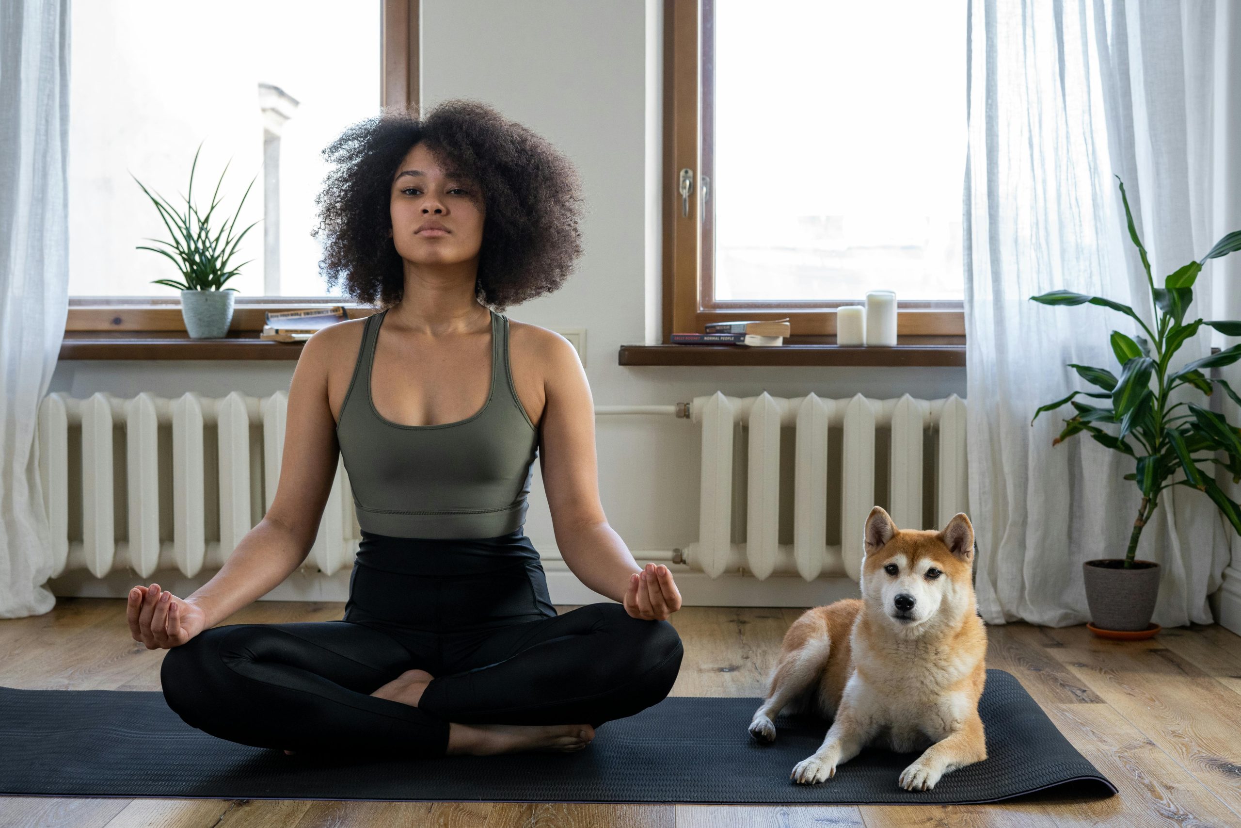 A woman meditating on a yoga mat while her dog lays beside her.