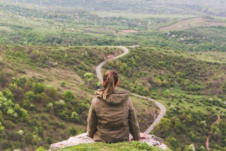 Woman sitting on edge looking out over a path.
