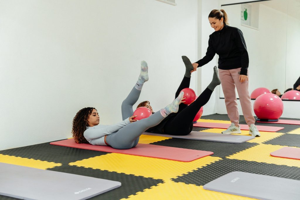 Two women on their backs doing an exercise with another woman coaching them through it.