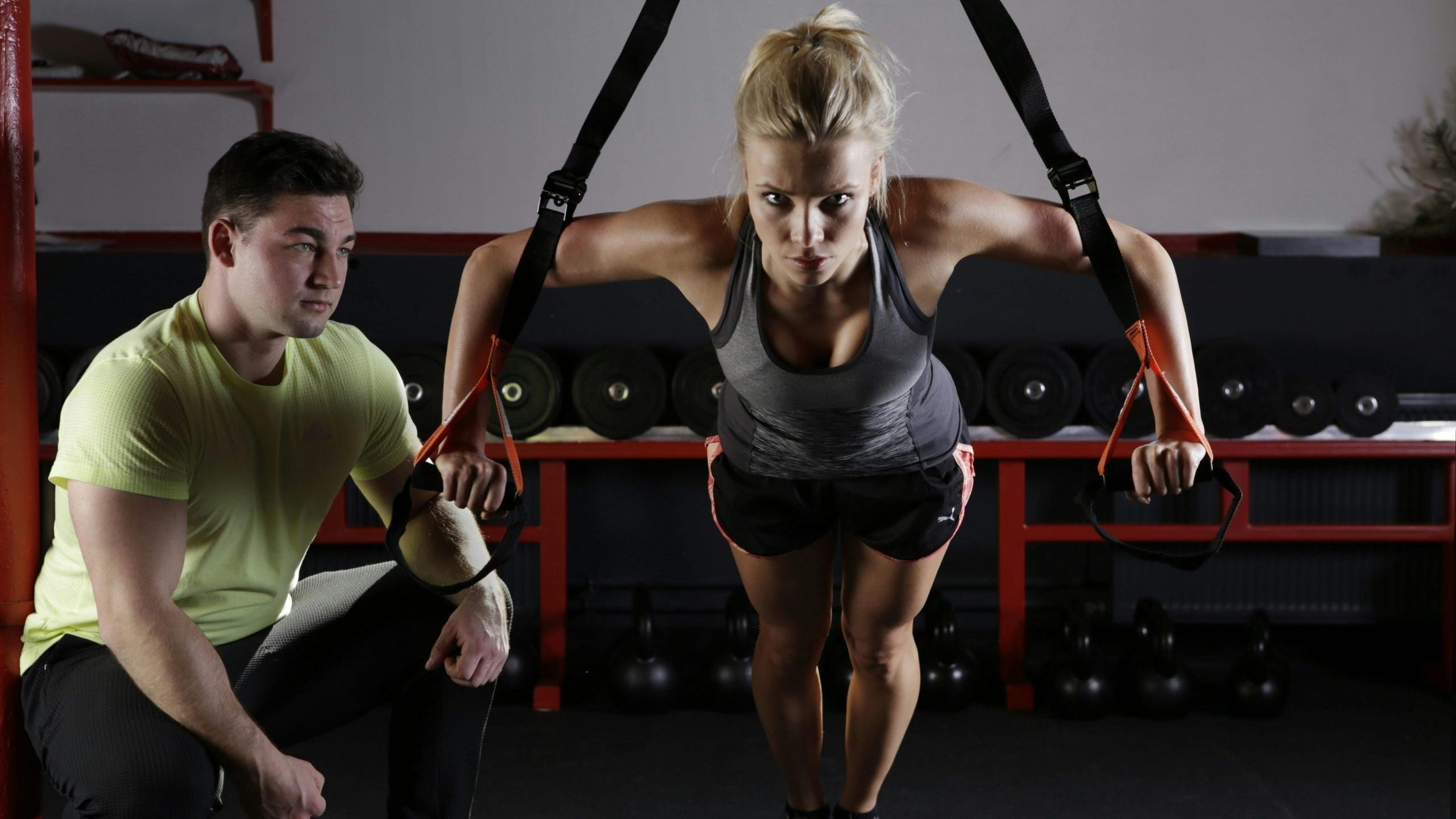 Male trainer kneeling next to female trainee as she does incline push-ups.
